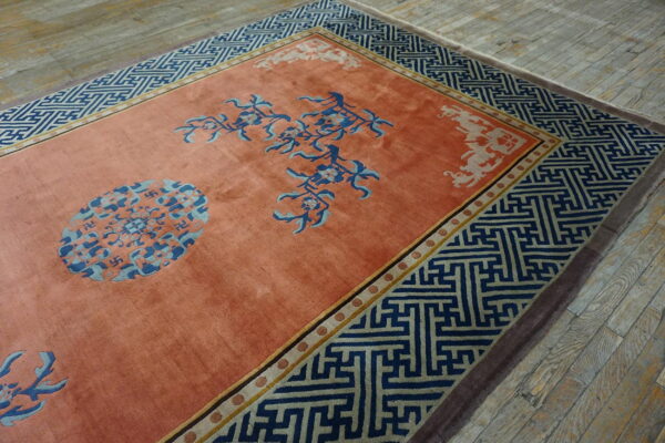 A salmon rug with navy greek key borders and blue floral medallions rests on weathered wood floors.