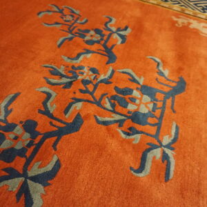 Plush orange rug featuring large navy and gray floral designs with a distinct geometric border.