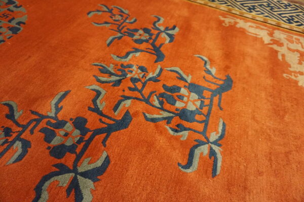 Plush orange rug featuring large navy and gray floral designs with a distinct geometric border.