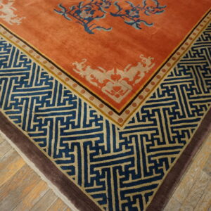 Close-up of an orange rug with blue and tan geometric borders on distressed wood flooring.