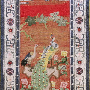 Red and orange rug with a peacock and crane pictorial design, bordered by navy blue and geometric white motifs.