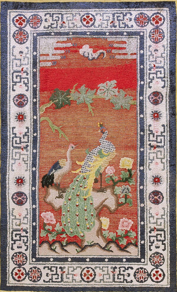 Red and orange rug with a peacock and crane pictorial design, bordered by navy blue and geometric white motifs.