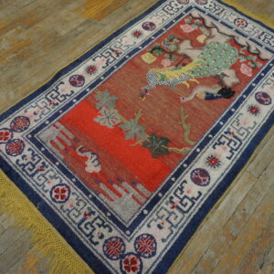Red rug with a blue and white border, featuring a colorful peacock design on worn wood planks.
