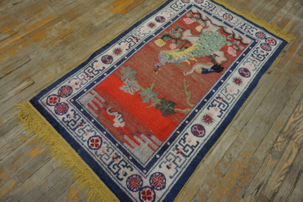 Red rug with a blue and white border, featuring a colorful peacock design on worn wood planks.