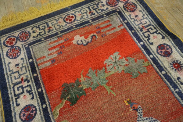 Red field rug with carved green leaves, blue and gray accents, a geometric border, and bright yellow fringe on wood.