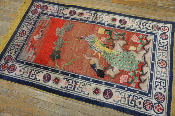 Red rug featuring a central peacock and floral design, blue borders, and yellow fringe on wood floor.