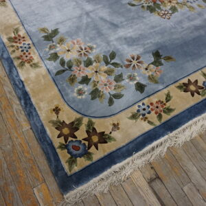 Lustrous light blue rug with colorful floral borders and fringe visible on distressed wood flooring.
