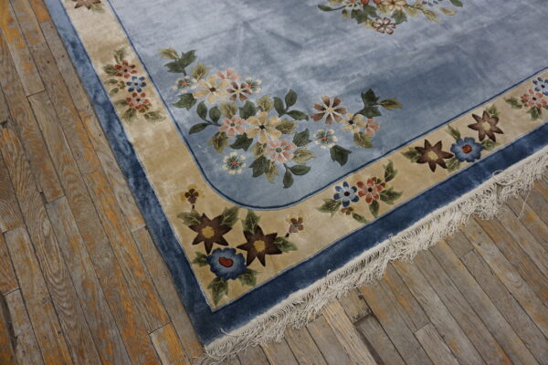 Lustrous light blue rug with colorful floral borders and fringe visible on distressed wood flooring.
