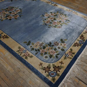 Low-pile blue rug with floral bouquets and a wide tan border lies on rustic, worn hardwood floors.
