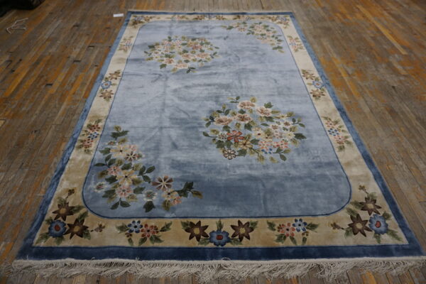 Velvety blue rug featuring pale floral medallions, a tan border, and fringe on distressed wooden floors.