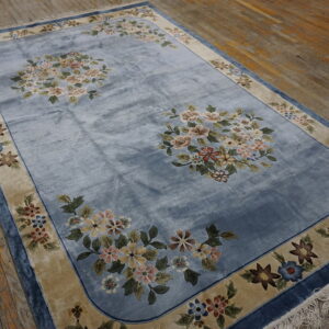 Plush blue rug featuring large floral arrangements and a beige border rests on rustic wood floors.