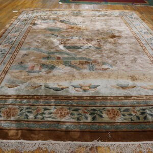 Muted beige rug with a detailed landscape pattern, carved borders, and white fringe on hardwood flooring.