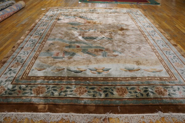 Muted beige rug with a detailed landscape pattern, carved borders, and white fringe on hardwood flooring.
