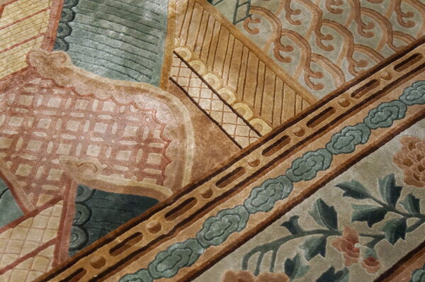 Close-up of a sculpted rug pattern featuring sage, tan, terracotta, and brown geometric and floral motifs.