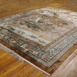 Beige area rug with ornate floral borders and a central landscape pattern rests on wood planks.