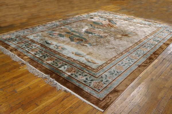 Beige area rug with ornate floral borders and a central landscape pattern rests on wood planks.