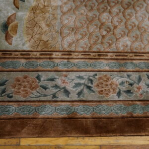 Sculpted, high-pile rug detail showing layered floral and cloud borders in sage green, tan, and brown on wood.