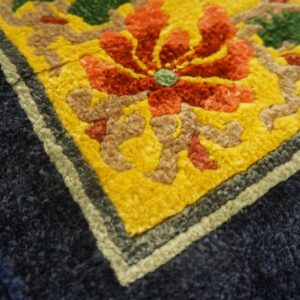 Vibrant close-up detail of a rug with a red flower, yellow field, and thick navy blue border.