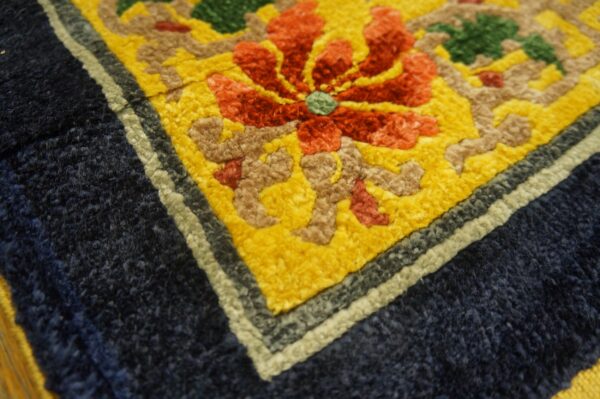 Vibrant close-up detail of a rug with a red flower, yellow field, and thick navy blue border.