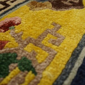 Sculpted high-pile rug detail showing yellow, brown, red, and green abstract patterns next to navy and cream borders.