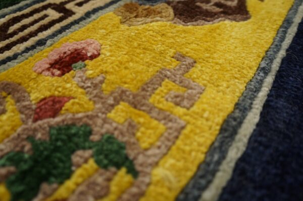Sculpted high-pile rug detail showing yellow, brown, red, and green abstract patterns next to navy and cream borders.
