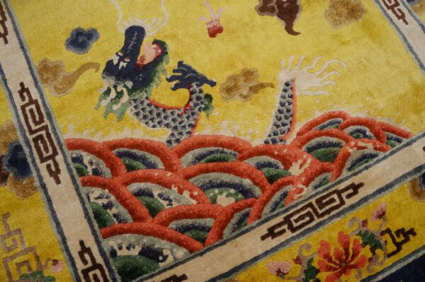 Textured yellow rug featuring a detailed blue dragon pattern, red waves, and a brown fretwork border.
