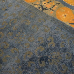 Medium pile blue rug with grey-green scrolling motifs and an orange and sage border detail on wood flooring.