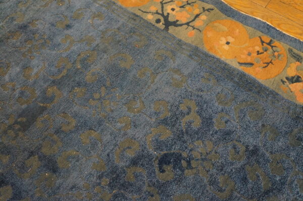 Medium pile blue rug with grey-green scrolling motifs and an orange and sage border detail on wood flooring.