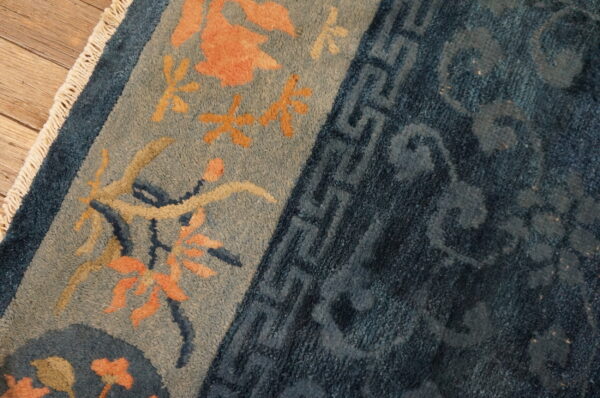 Close-up of blue rug borders featuring peach florals and dark geometric motifs on light wood flooring with visible fringe.