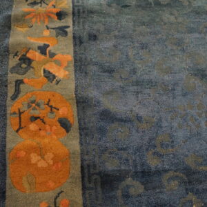 Close-up of a blue rug featuring an orange and gray floral border on distressed wood flooring.
