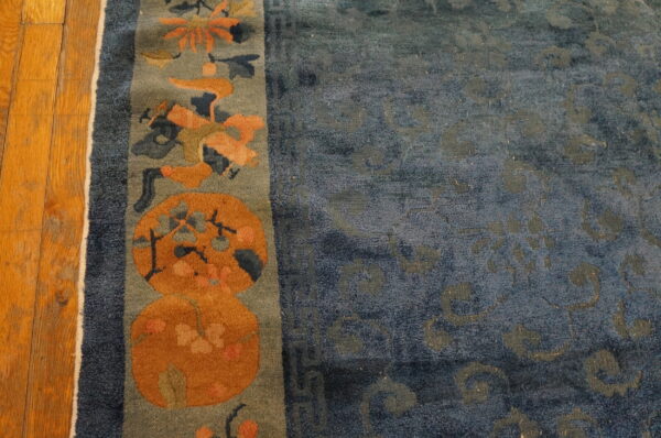 Close-up of a blue rug featuring an orange and gray floral border on distressed wood flooring.