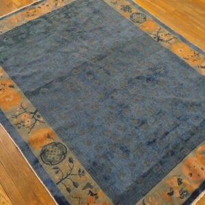 Distressed blue low-pile rug featuring a wide border of orange medallions and sage floral patterns on hardwood flooring.