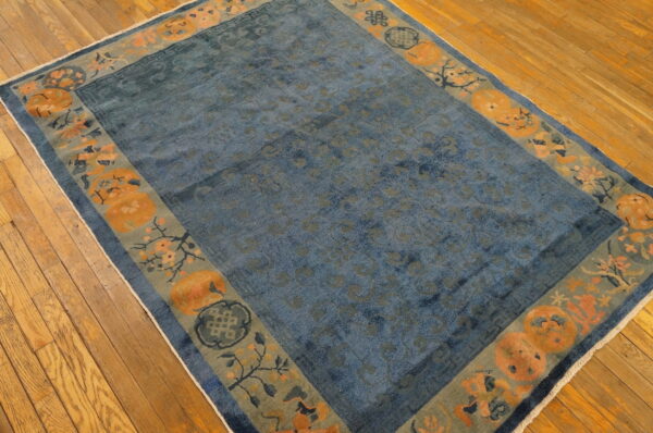 Distressed blue low-pile rug featuring a wide border of orange medallions and sage floral patterns on hardwood flooring.