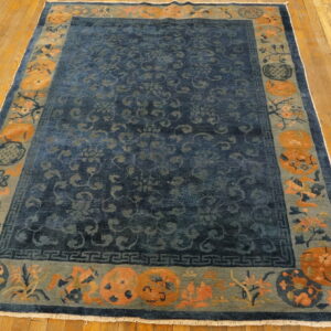 Dark blue low-pile rug featuring a wide border of orange and sage green botanicals on light wood planks.