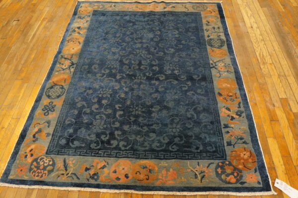Dark blue low-pile rug featuring a wide border of orange and sage green botanicals on light wood planks.