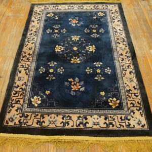 Deep blue rug with gold floral designs and complex beige borders lies on rustic wood flooring.
