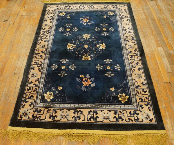 Deep blue rug with gold floral designs and complex beige borders lies on rustic wood flooring.
