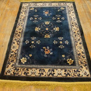 Dark blue floral rug with yellow and tan borders resting on distressed plank wood flooring.