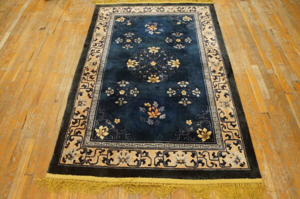 Dark blue floral rug with yellow and tan borders resting on distressed plank wood flooring.