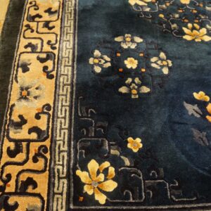 Deep blue high-pile rug with yellow and orange floral patterns and a wide tan border on light wood floors.