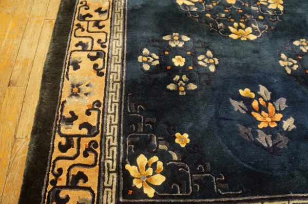 Deep blue high-pile rug with yellow and orange floral patterns and a wide tan border on light wood floors.