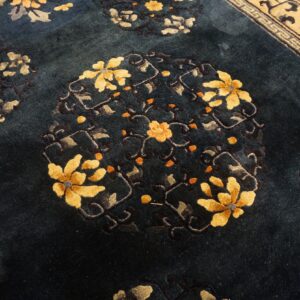 Dark blue pile rug featuring large yellow and orange floral medallions beside a tan geometric border.