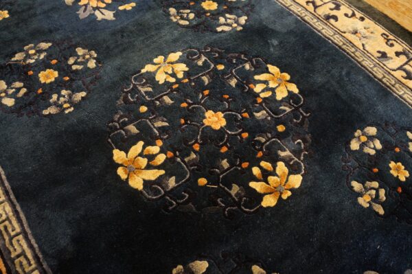 Dark blue pile rug featuring large yellow and orange floral medallions beside a tan geometric border.