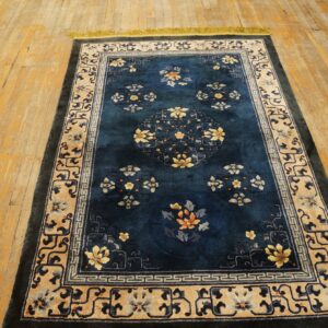 A deep blue rug with yellow and orange floral patterns and detailed beige borders rests on a light wood floor.