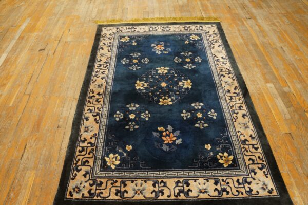 A deep blue rug with yellow and orange floral patterns and detailed beige borders rests on a light wood floor.