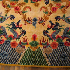 Multicolor rug featuring detailed gold and blue dragon motifs, clouds, and waves on a yellow background over wood flooring.