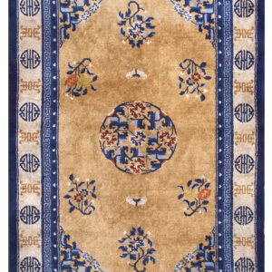 A golden tan rug with navy and beige borders features a central medallion and scattered blue floral sprays.