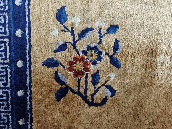Close-up of a high-pile tan rug featuring a central blue and rust floral motif and a dark blue border.