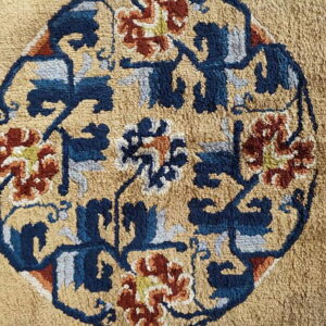 Textured tan rug detail with a central oval motif patterned in navy, rust, and light blue.