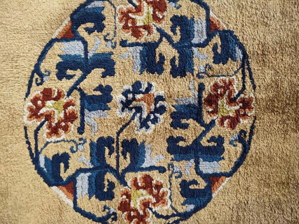 Textured tan rug detail with a central oval motif patterned in navy, rust, and light blue.
